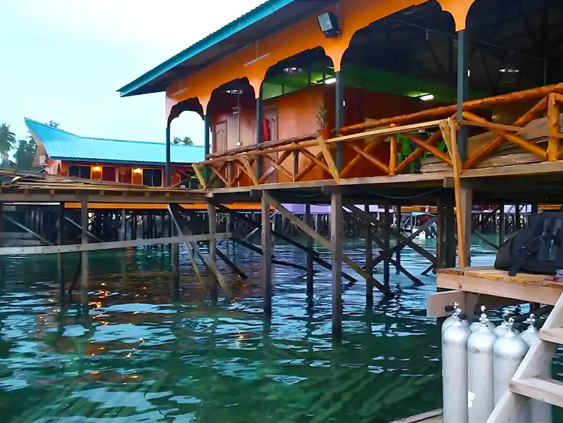 Arung Hayat's longhouse homestay sitting above Mabul's clear turquoise waters, with scuba tanks ready for the next day's dive into Sipadan's wonders.