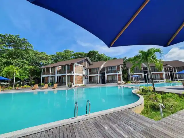 Expansive resort swimming pool and wooden sun deck in front of the modern Pool Villa buildings at Borneo Divers Mabul Resort in Sabah.