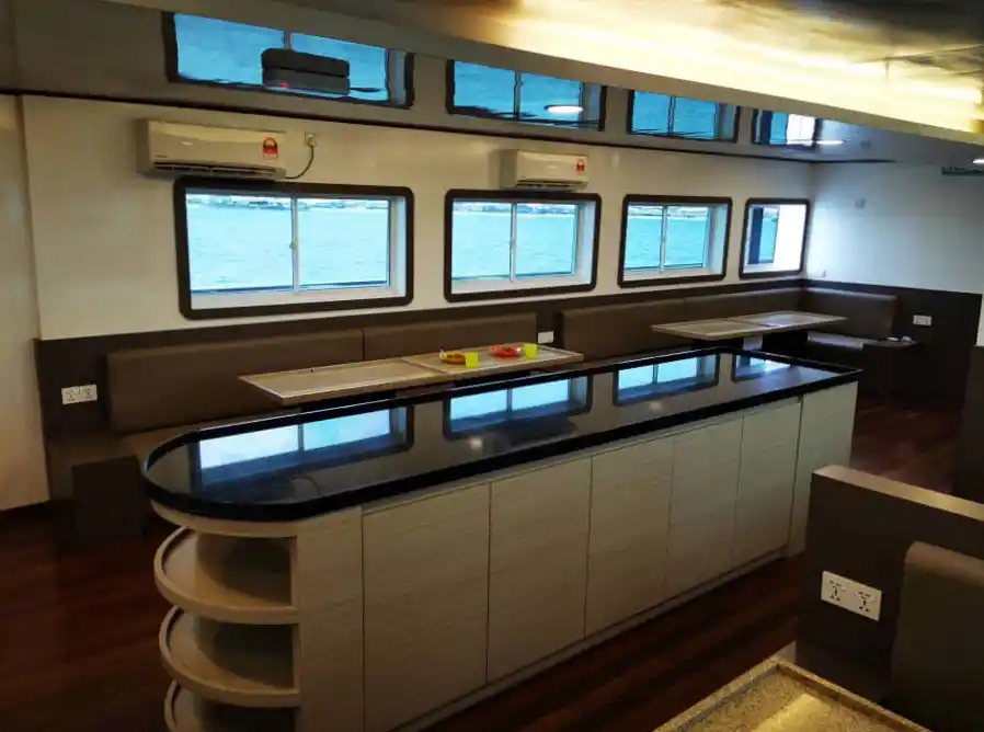 Brightly lit indoor lounge and dining hall on the Celebes Explorer 9 (CE9) liveaboard, with ample booth seating for meals and briefings.