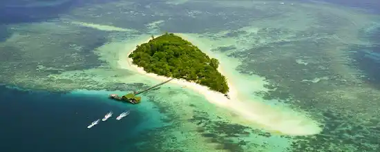 Breathtaking sky view of Lankayan Island, showing the lush island, extensive coral reef, and dive boats heading out for an adventure in the Sulu Sea.
