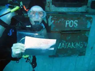 Scuba diver mailing a postcard from the unique Underwater Post Office at Mataking Island Resort, a fun novelty for a 5-star diving holiday.