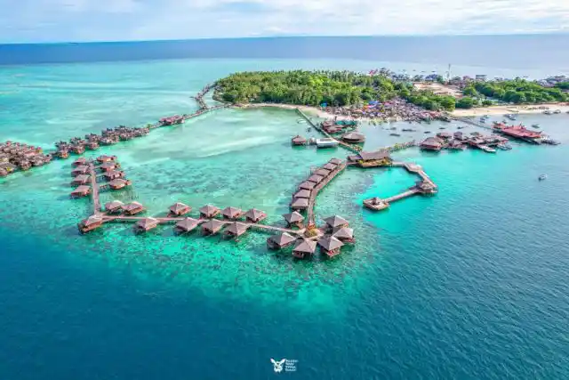 Spectacular high-altitude drone panorama of Mabul Island, showing the luxurious Sipadan Water Village in the foreground and the rest of the island's resorts and villages.