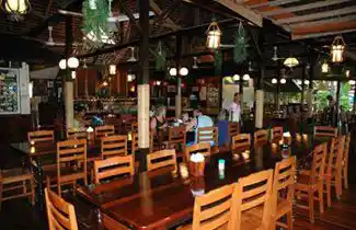 Guests enjoying a meal in the spacious, open-air dining hall of Sipadan-Mabul Resort, with its rustic wooden tables and high ceilings.