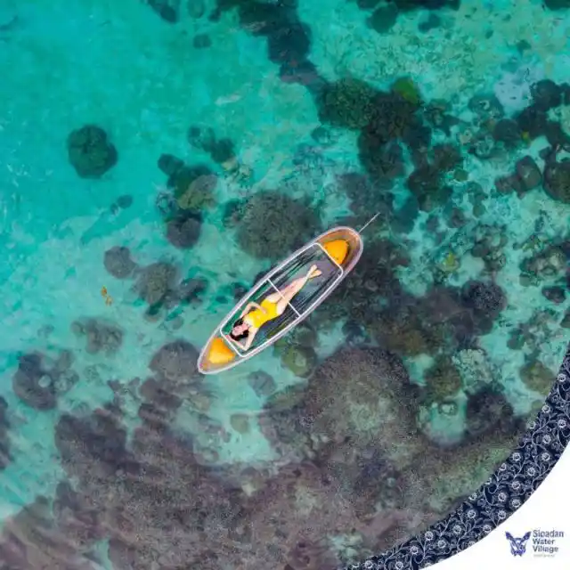 Guest relaxing in a transparent kayak, looking down at the beautiful coral reef below in the crystal-clear waters of Sipadan Water Village.