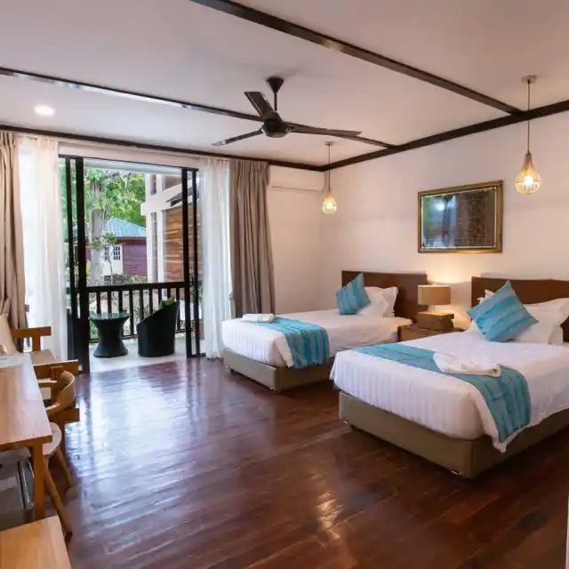 Bright twin-bed villa room at Sipadan Sabah Resort features polished wood floors, balcony seating and restful space for divers between adventures.
