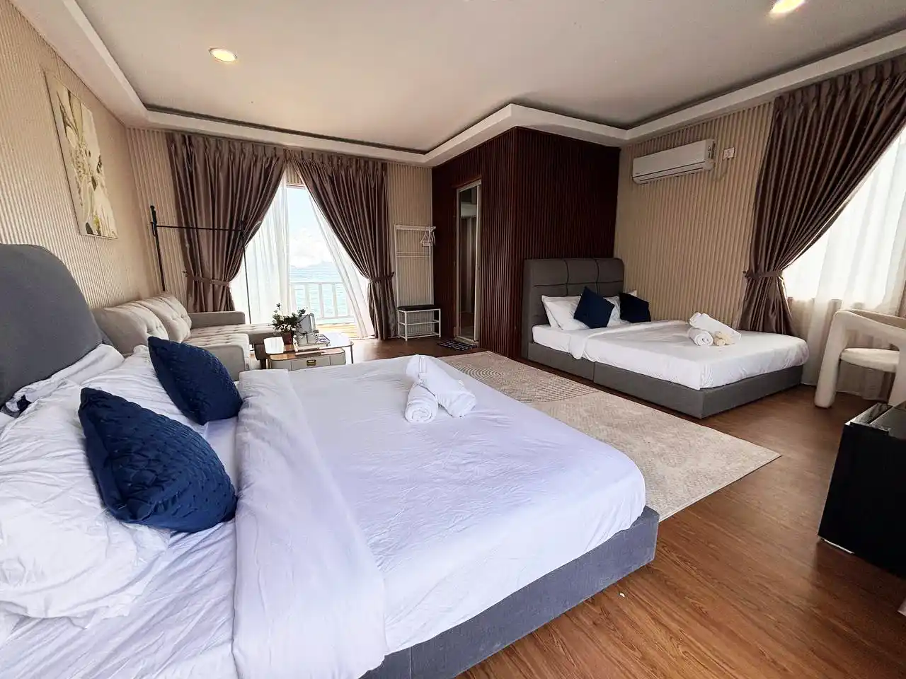 Spacious and modern family room at Blue Ocean Resort, well-appointed with two double beds, a sofa, and large windows with a sea view.