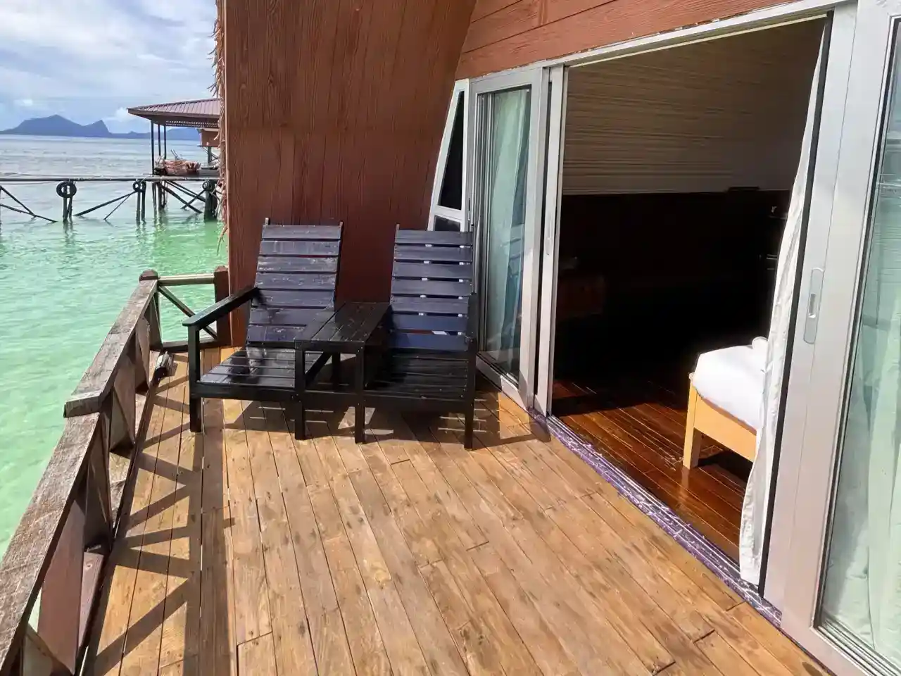 Private wooden balcony of an overwater chalet at Crystal Resort, with chairs overlooking the clear green waters near Semporna.
