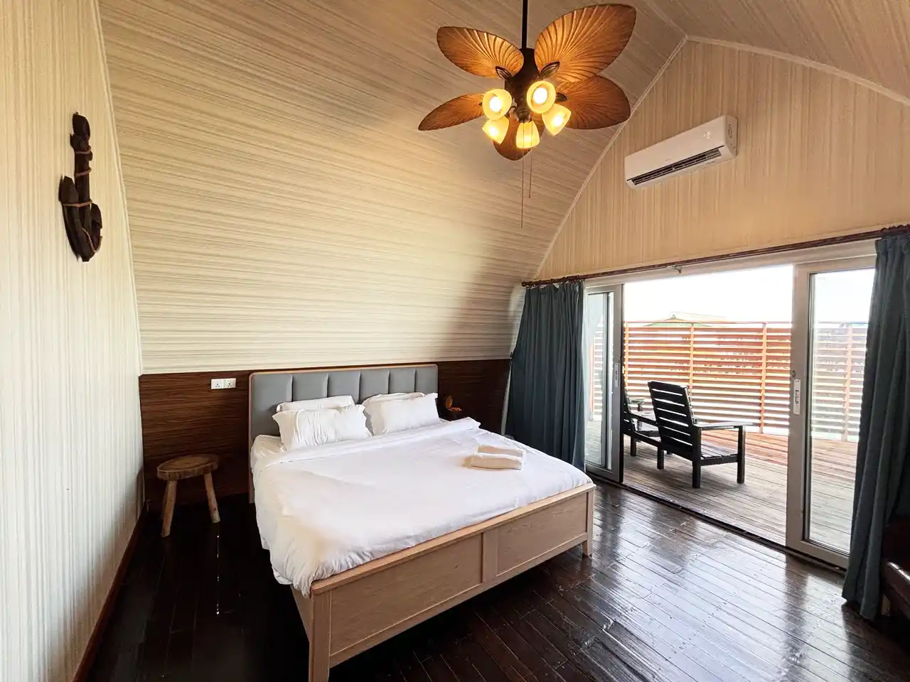 Bright and airy bedroom in an overwater villa at Crystal Resort, featuring a vaulted ceiling and a large glass door opening to a private sundeck.