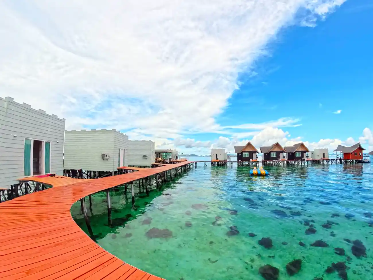 Winding orange boardwalk connecting the unique overwater chalets at Danglai Resort, a peaceful escape in the turquoise waters near Semporna.