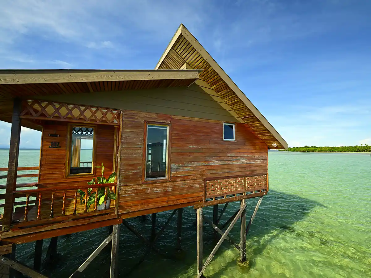 Beautiful wooden overwater chalet at Larapan Water Village, offering ocean and island views from its private balcony over the clear green sea.