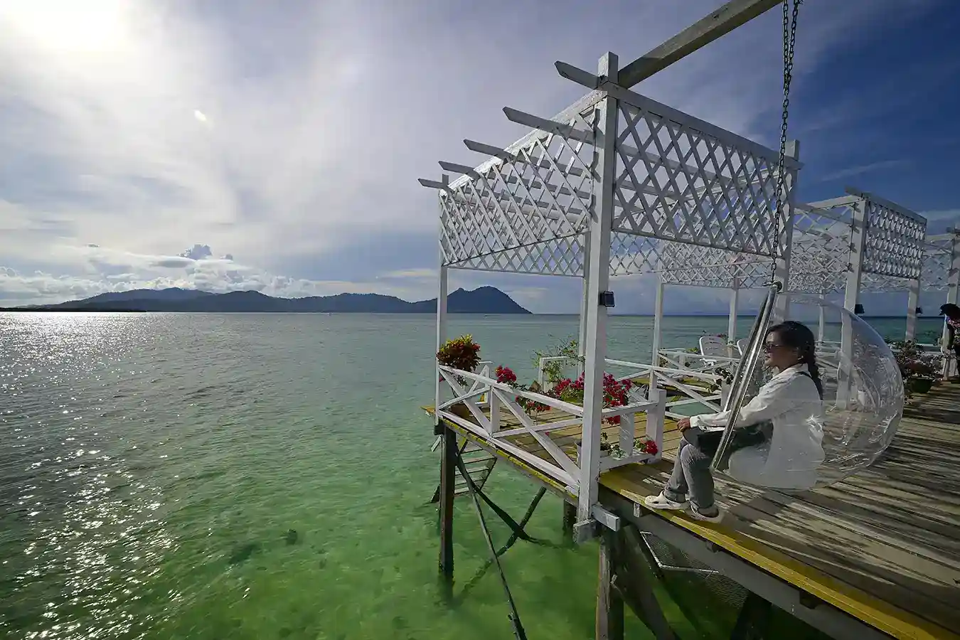 Guest relaxing in a unique bubble swing on the jetty at Larapan Water Village, enjoying the serene view of Bohey Dulang.
