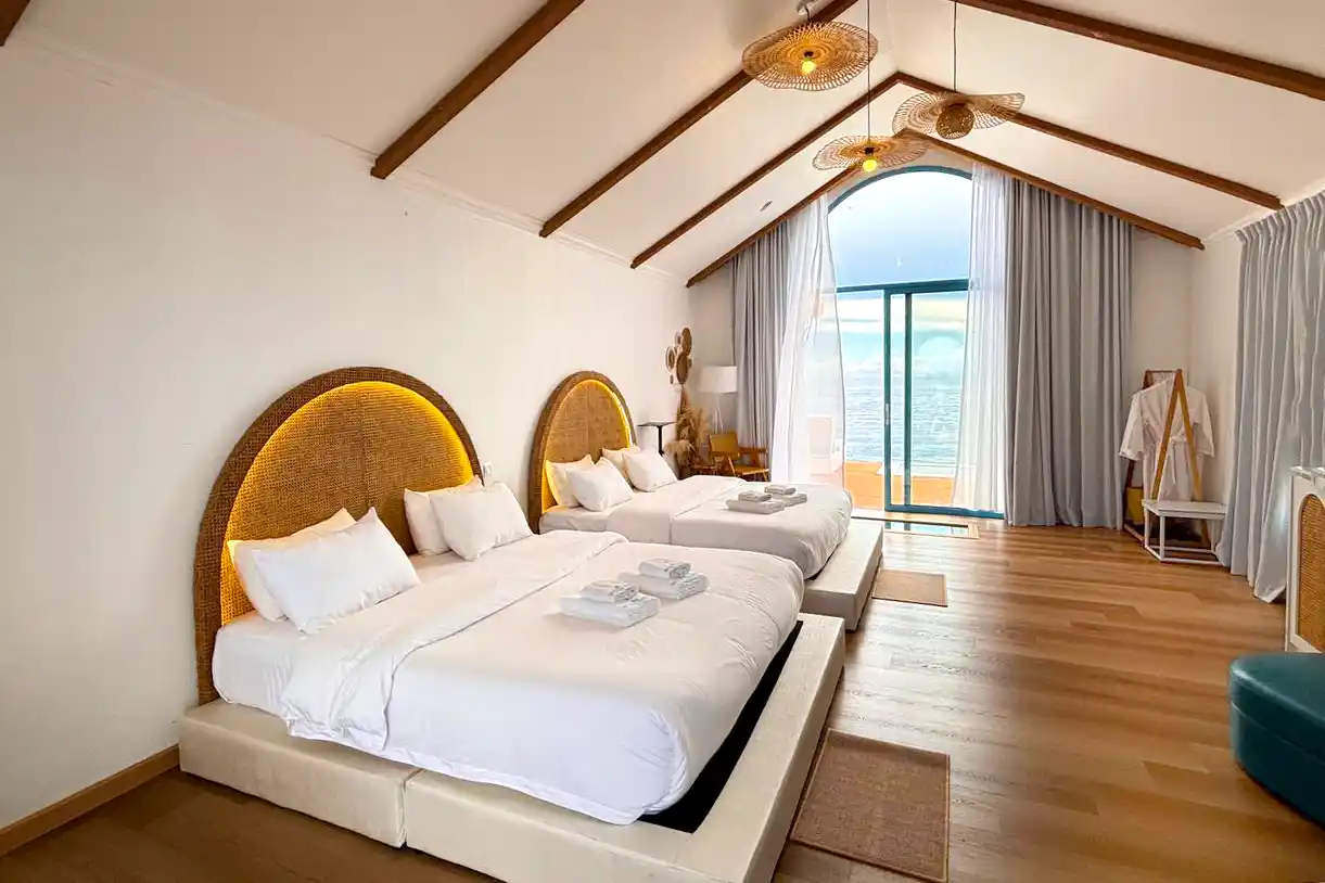Beautifully styled room at Royal Resort Semporna, featuring two large beds with illuminated wicker headboards and a spacious, open-plan layout under a vaulted ceiling.