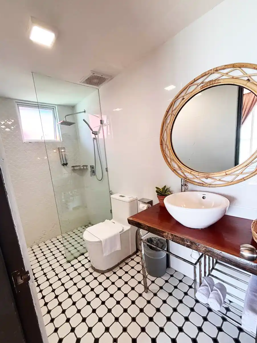 Stylish modern bathroom at Sand Bay Resort, featuring decorative floor tiles, a glass walk-in shower, and a rustic wooden vanity with a wicker mirror.