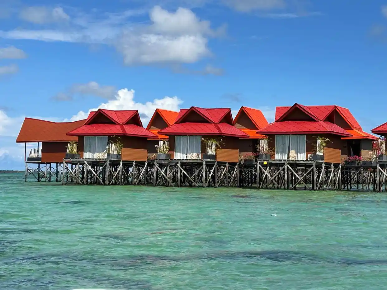 Colorful overwater chalets with bright red roofs at Sand Bay Resort, standing in the clear turquoise waters near Semporna.