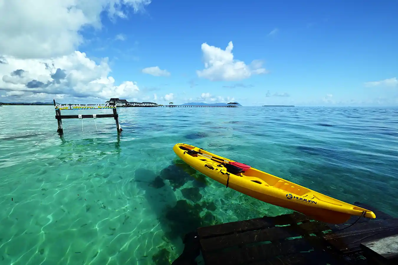 Bright yellow sea kayak floating in the crystal-clear turquoise water at Sky Water Villas, ready for exploring the shallow reefs.