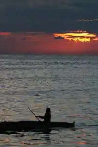 Local fisherman in a traditional boat silhouetted against a spectacular fiery sunset over the sea at Mabul Island, reflecting the local culture.
