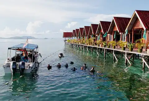 Scuba divers in the water preparing for a dive right off the jetty of Uncle Chang's dive lodge, a popular backpacker resort on Mabul island.
