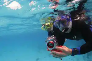 Students practicing with an underwater camera during a PADI specialty photography course in the clear blue waters of Mabul island.